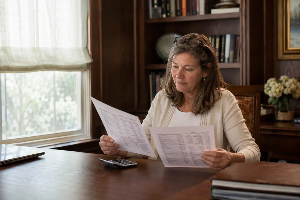 Woman reviewing a Medicare Part B premium statement at a home desk, calculator and papers nearby, soft daylight.